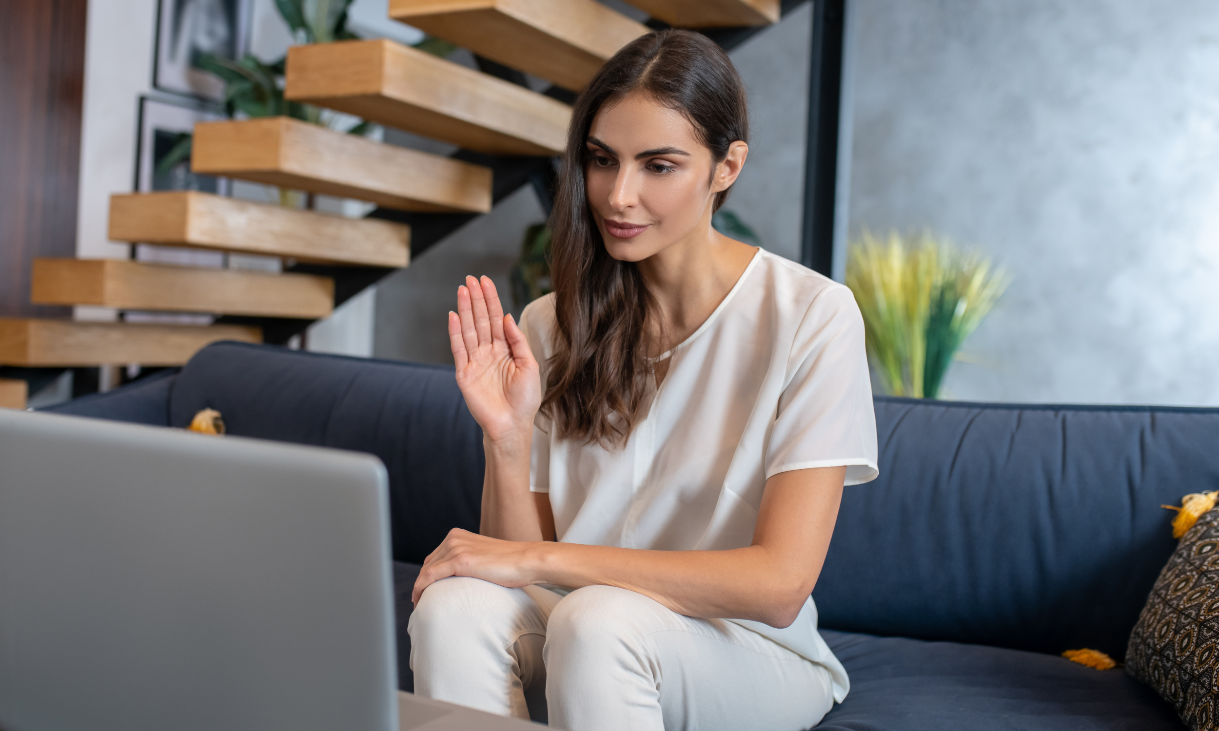 A woman sitting on a couch with her hands raised, engaged in an online therapy session