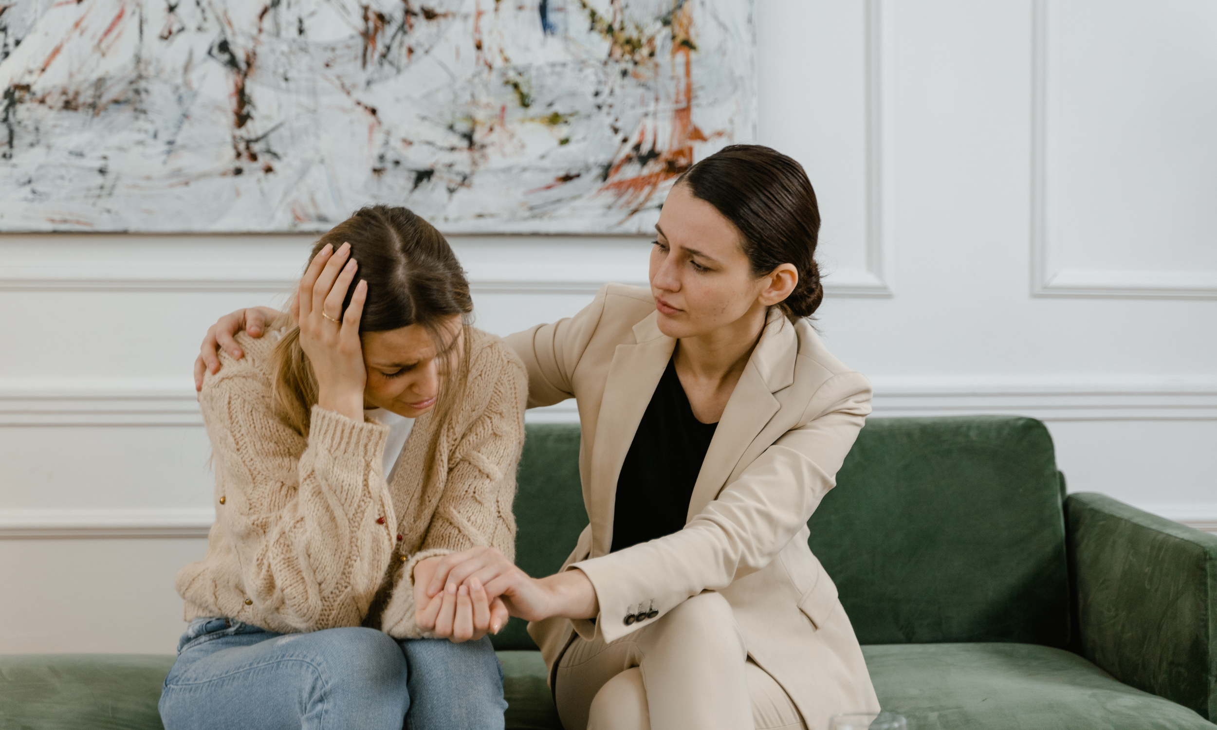 Two women sitting on a couch in a therapy center, gently holding hands and sharing a supportive moment.